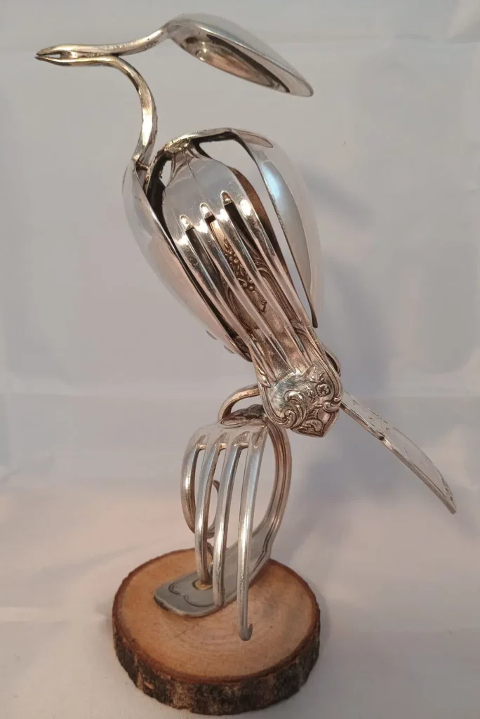 Sculpture oiseau en métal recyclé réalisée avec couverts anciens et pièces métalliques polies